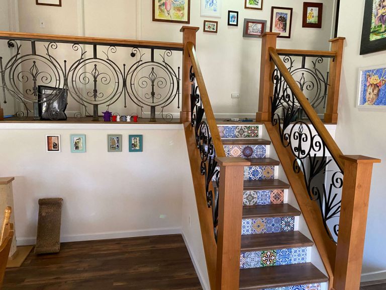 A staircase with hand crafted wooden railings and decorative tile risers leading to an upper floor with custom designed wrought iron railing accents.