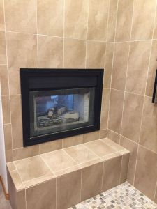 Bathroom features shower with tiled wall, a matching tiled ledge to sit on. Above the ledge is a gas fireplace built into the shower wall.