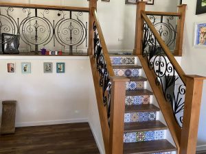 A staircase with hand crafted wooden railings and decorative tile risers leading to an upper floor with custom designed wrought iron railing accents.