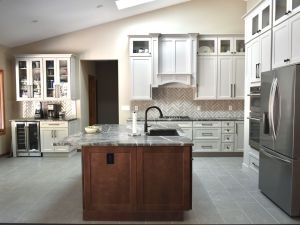 Very large modern kitchen with custom white cabinetry along two walls. A gas stove is built into a quartz counter along one wall. A second wall includes floor to ceiling cabinets with a built in oven, microwave and refrigerator. The side of the kitchen features a large picture window, flanked by separate floor to ceiling cabinetry with mullion glass panels and a wine cabinet below.